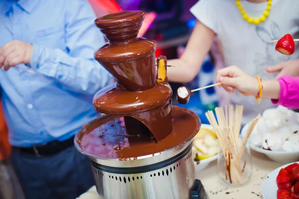 Vibrant Picture of Chocolate Fountain Fontain on childen kids birthday party with a kids playing around and marshmallows and fruits dip dipping into fountain — Stock Photo, Image