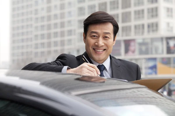 Hombre de negocios sonriendo, trabajando al aire libre en el coche — Foto de Stock