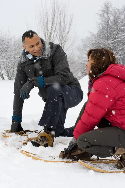 Pareja agachándose en la nieve usando raquetas de nieve — Foto de Stock