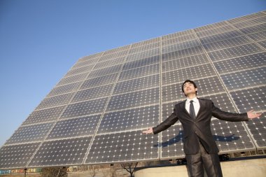 Businessman with arms outstretched in front of solar panels clipart
