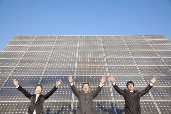 Businesspeople with Arms Outstretched in front of Solar Panel Stock Image