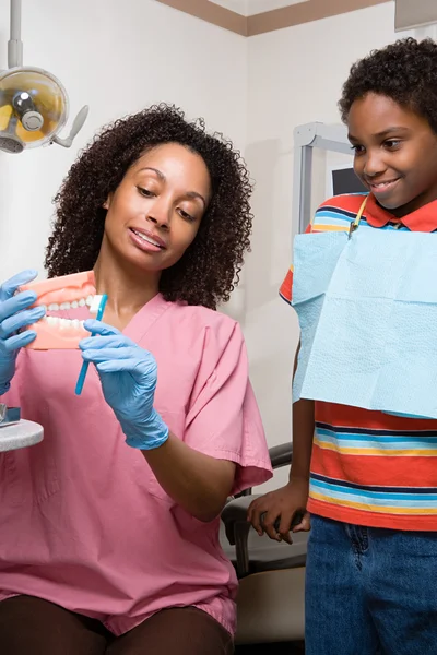 Dental nurse showing boy how to clean teeth properly — Stock Photo, Image