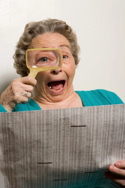 Woman reading newspaper with magnifying glass — Stock Photo, Image