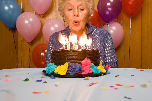 Senior woman blowing out candles on cake — Stock Photo, Image