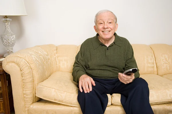 Oudere man op de Bank met de afstandsbediening — Stockfoto