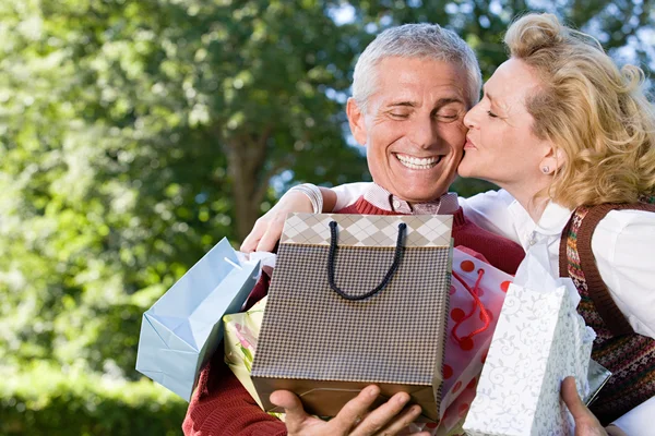 Жена целует мужа с пакетами подарков — стоковое фото