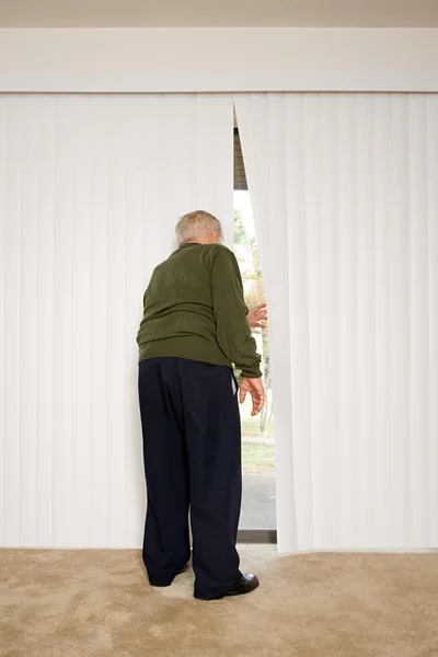 Elderly man looking out of blinds — Stock Photo, Image