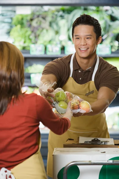 Sales assistants handing packets of apples — Stock Photo, Image
