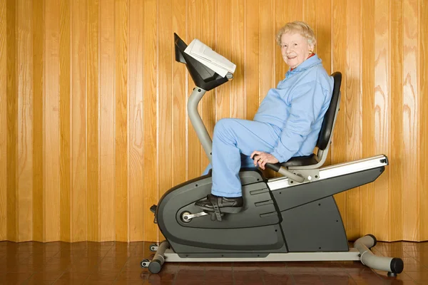 Äldre kvinna på en motionscykel — Stockfoto