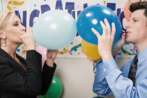 Two office workers blowing up balloons — Stock Photo, Image