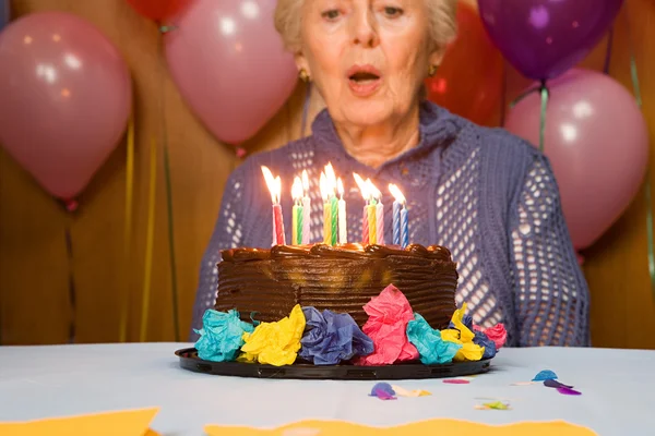 Senior woman blowing out candles on cake — Stock Photo, Image