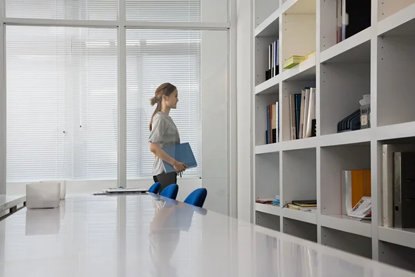 Woman in office looking on bookshelves — Stock Photo, Image