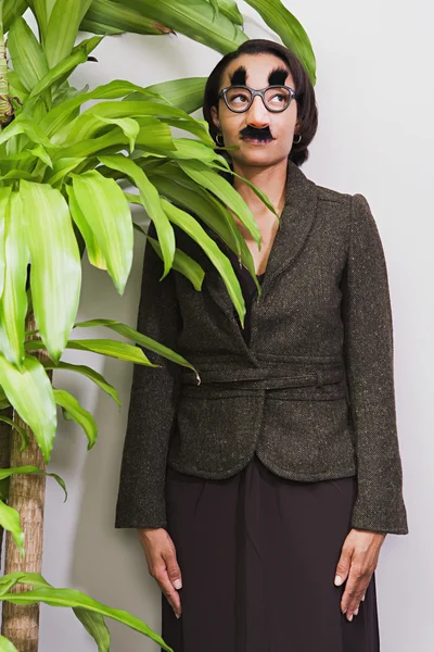 Businesswoman hiding behind plant wearing disguise — Stock Photo, Image