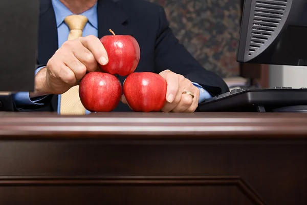 Бизнесмен балансирует яблоки на столе — стоковое фото