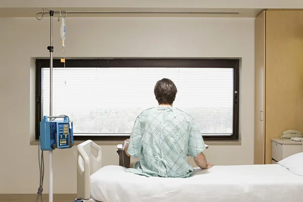 Пациент на капельнице сидит на кровати — стоковое фото