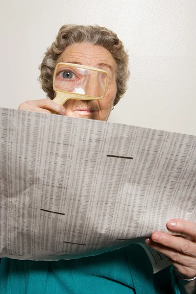 Woman reading newspaper with magnifying glass — Stock Photo, Image