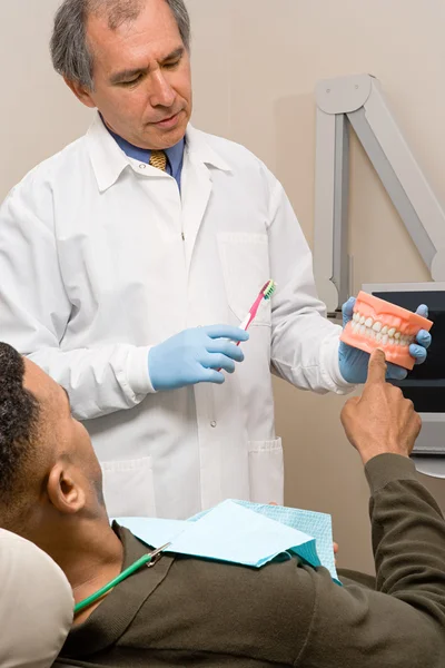 Dentist showing patient how to clean teeth — Stock Photo, Image