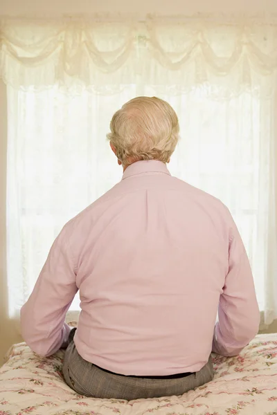 Oudere man zit op een bed — Stockfoto