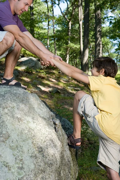Father pulling son onto rock — Stock Photo, Image