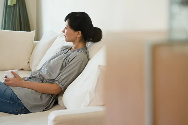 Kvinnan tänker sitter på soffan — Stockfoto