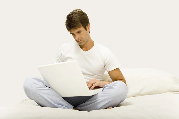 Dizüstü bilgisayar kullanarak yatağın üstüne oturan adam — Stok fotoğraf
