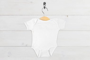 Küçük tahta bir askıda asılı beyaz bebek tulumu modern beyaz tahta bir duvara karşı.
