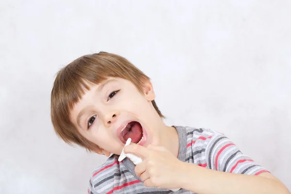 Um menino aplica um spray de garganta para aliviar uma dor — Fotografia de Stock