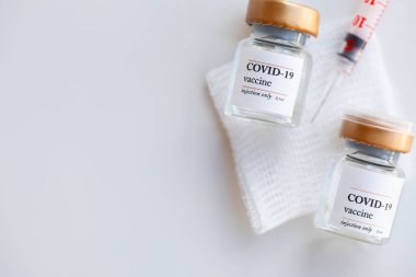 Steril gause bezi üzerinde COVID-19 aşısı olan iki şişe. Arka planda şırınga var. Düz yatıyordu