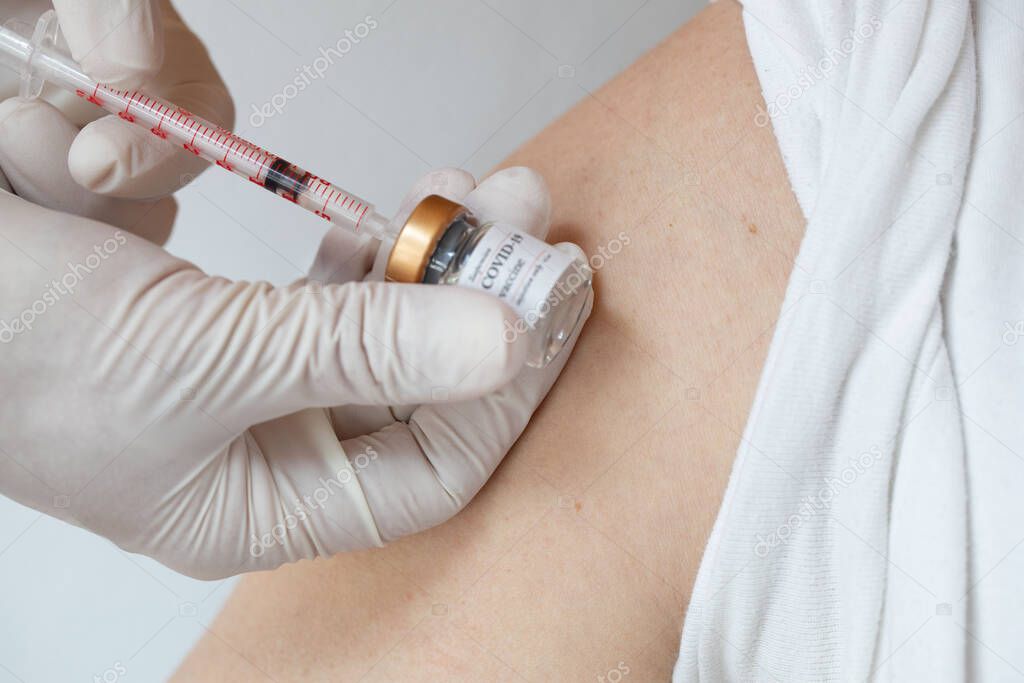 Open shoulder of the man before vaccination. Medical assistant preparing the syringe in the background.