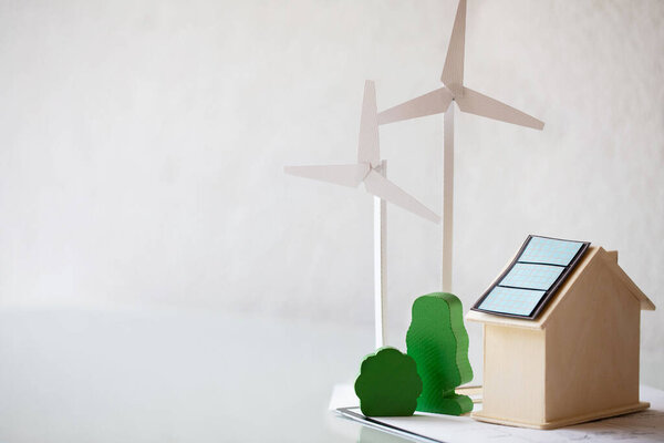 Paper model of wind turbine , green trees , wooden house with solar panels on the table. Closeup