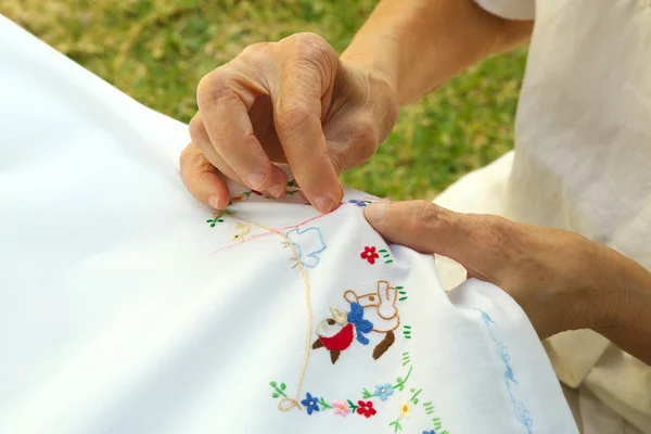 An old woman is embroidering on the white blanket — Stock Photo, Image