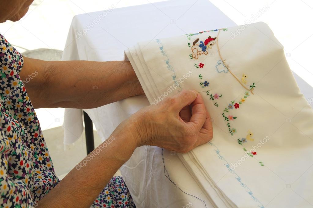 An old woman between 70 and 80 years old is embroidering on a wh