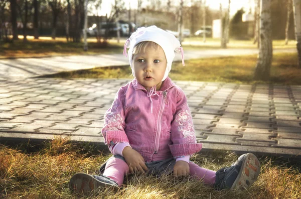 かわいい女の子は黄色の秋の草の上に座っています。 — ストック写真