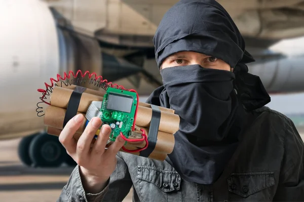 Terrorism concept. Terrorist in airport holds dynamite bomb in hand — Stock Photo, Image