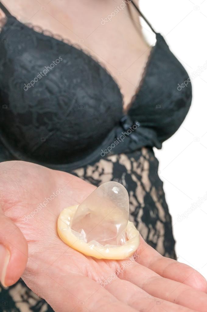 Sexy woman in black nightdress holds condom in hand.