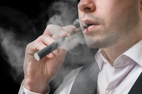 Homem caucasiano jovem está vaporizando com cigarro eletrônico ou vaporizador . — Fotografia de Stock