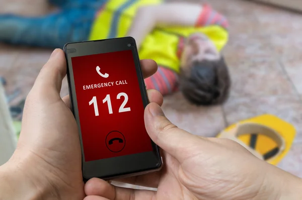 Numéro d'urgence (112) sur smartphone. Travailleur blessé a eu un accident du travail et est couché sur le sol . — Photo