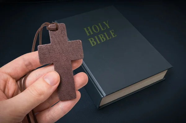 La mano sostiene la cruz de madera sobre la Santa Biblia . —  Fotos de Stock