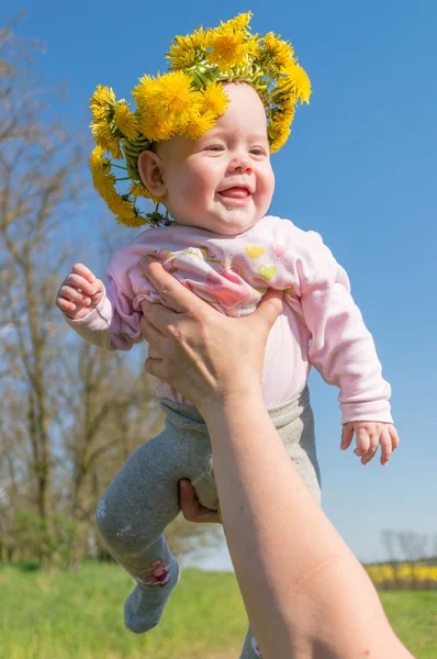 Padre sostiene a su bebé. Feliz bebé tiene corona de diente de león en la cabeza — Foto de Stock