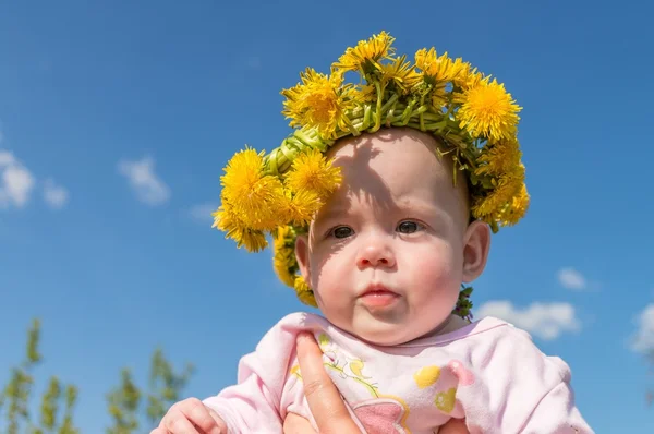 Childhood concept. Happy baby has dandelion wreath on head. — Stock Photo, Image