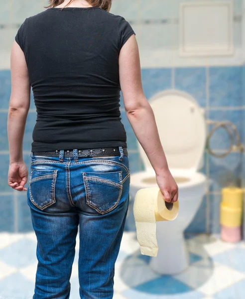 Mujer sufre de diarrea tiene papel higiénico en la mano en el baño . — Foto de Stock