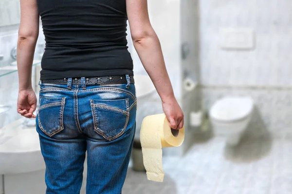 Woman suffers from diarrhea holds toilet paper in hand in restroom. — Stock Photo, Image