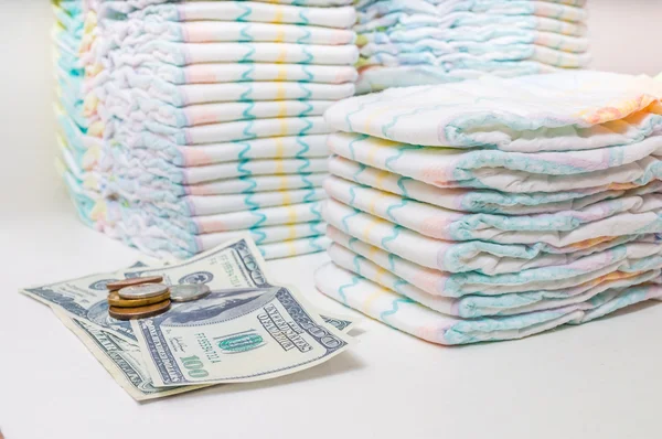 Cuidados infantis caros. Uma pilha de fraldas e dinheiro em fundo branco — Fotografia de Stock