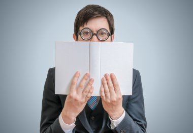 Genç utangaç adam okuma ve kitap beyaz kapaklı arkasında yüzünü saklıyor.