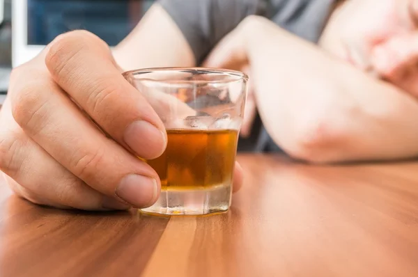 Alcoholic man is sleeping on table. Glass with alcohol in hand.