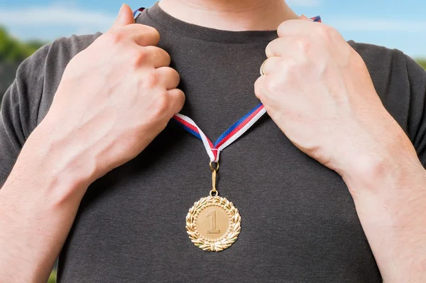 Sportsman (um vencedor) está colocando medalha de ouro em seu peito . — Fotografia de Stock