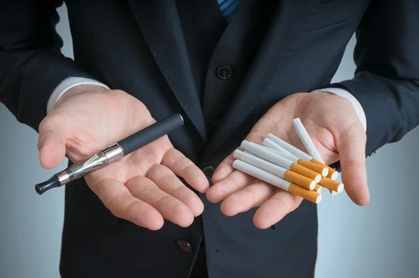 Homem está segurando vaporizador e cigarros de tabaco convencionais e comparando ou oferecendo . — Fotografia de Stock