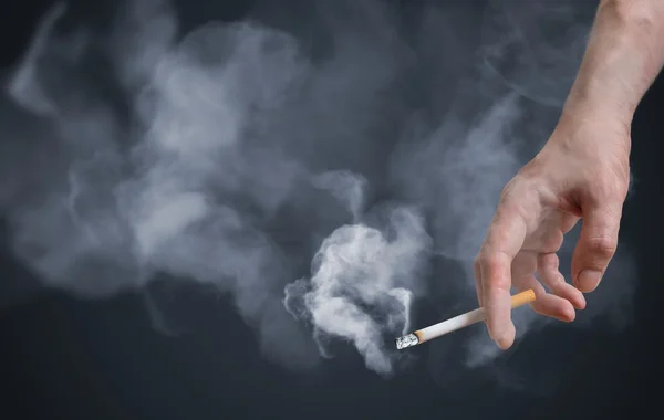 Курець тримає куріння сигарет в руці. Багато диму навколо — стокове фото