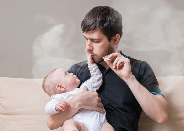 Bad father is smoking and holding little baby in hands. — Stock Photo, Image