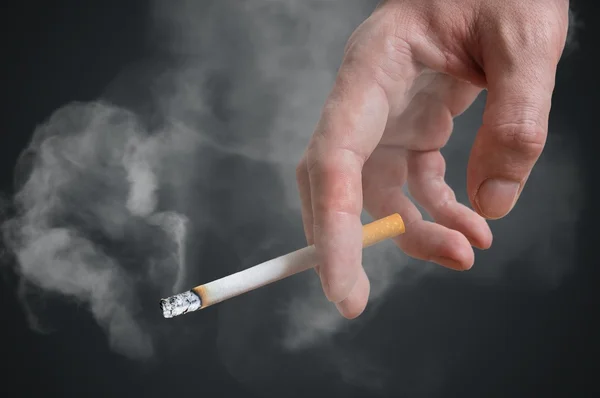 Человек (курильщик) держит сигарету в руке на черном фоне. Дым вокруг . — стоковое фото